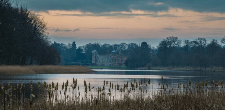 Image of the serene Blickling Hall Estate lake, surrounded by lush greenery and beautiful architecture.