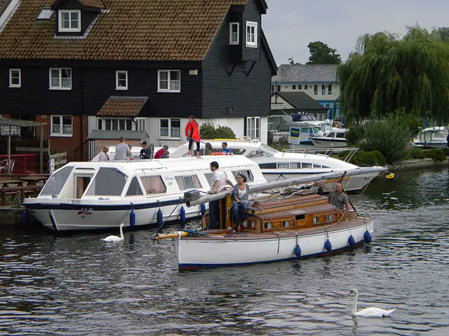 A Wroxham day boat hire, docked by a wooden pier on the calm waters of the Norfolk Broads.
