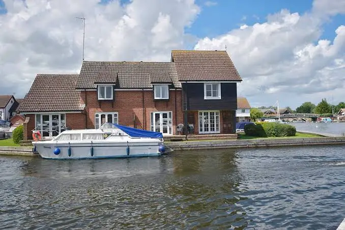 "Image of Peninsula Cottages nestled along the picturesque landscape of Wroxham within the Norfolk Broads. The cottages sit amid lush greenery, offering a charming retreat in this renowned Norfolk Broads wroxham destination."