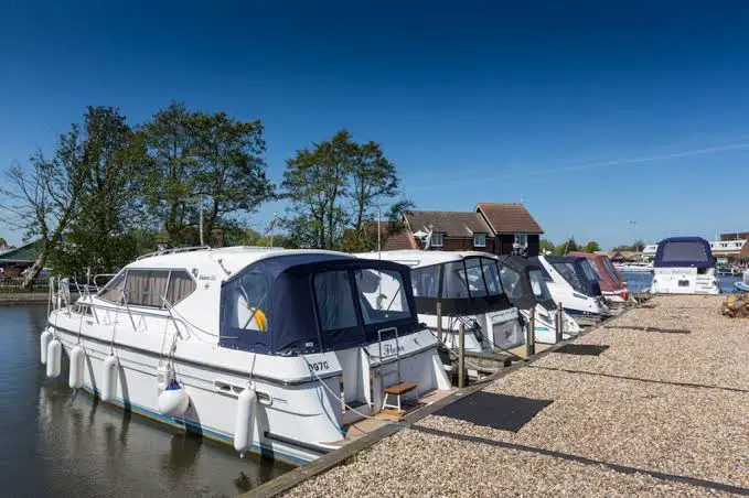 "Image of the free moorings in Wroxham within the Norfolk Broads, offering a serene docking spot along the banks of the River Bure. Boats are peacefully anchored, surrounded by the scenic beauty of the Norfolk Broads at Wroxham."